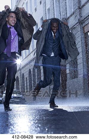 Stock Photo - Happy businessmen covering heads with coats in rainy street. Fotosearch