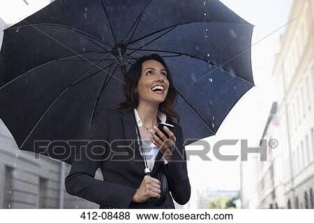 Happy businesswoman text messaging with cell phone under umbrella in rain View Large Photo Image Stock Photo - Happy businesswoman text messaging with cell phone under umbrella in rain. Fotosearch