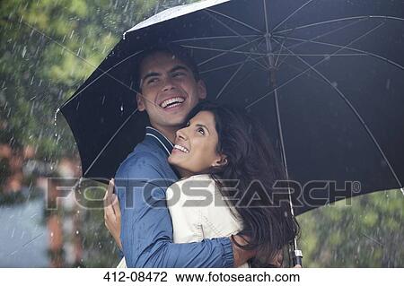 Happy couple hugging under umbrella in rain View Large Photo Image Stock Image - Happy couple hugging under umbrella in rain. Fotosearch