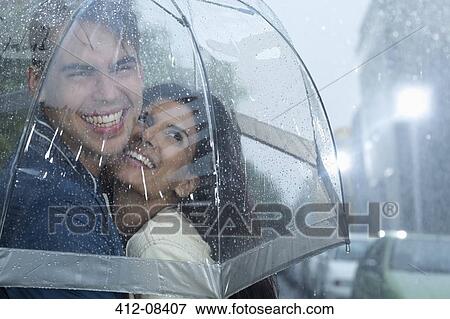 Stock Photo - Happy couple hugging under umbrella in rain. Fotosearch