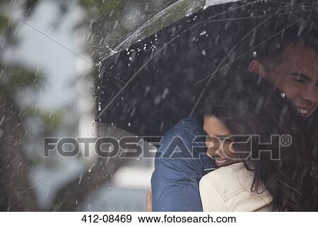 Stock Photo - Happy couple hugging under umbrella in rain. Fotosearch