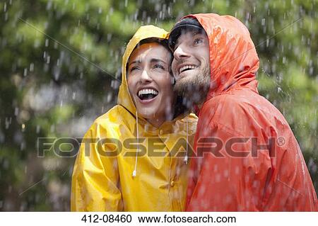 Happy couple in raincoats looking up at rain View Large Photo Image Stock Image - Happy couple in raincoats looking up at rain. Fotosearch