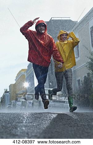 Happy couple in raincoats running down street in rain View Large Photo Image Stock Photo - Happy couple in raincoats running down street in rain. Fotosearch
