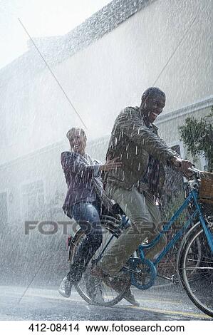 Picture - Happy couple riding bicycle in rainy street. Fotosearch