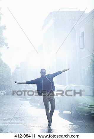 Stock Image - Happy man with arms outstretched in rainy street. Fotosearch