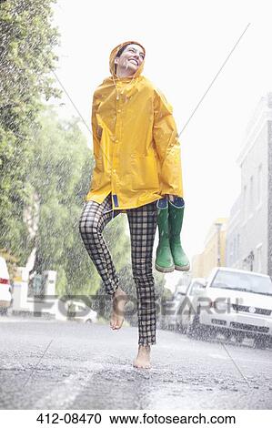 Stock Image - Happy woman dancing barefoot in rainy street. Fotosearch