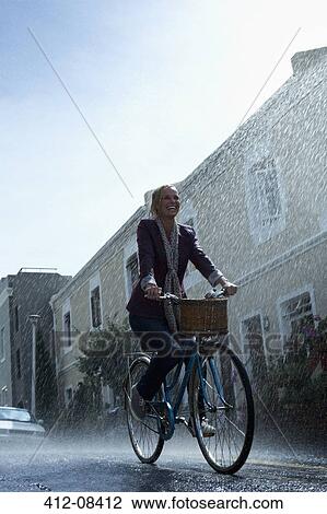 Happy woman riding bicycle in rainy street View Large Photo Image Stock Image - Happy woman riding bicycle in rainy street. Fotosearch