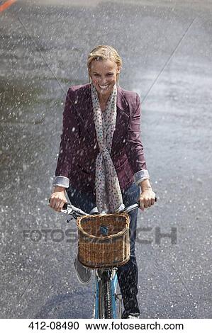 Happy woman riding bicycle in rainy street View Large Photo Image Stock Image - Happy woman riding bicycle in rainy street. Fotosearch