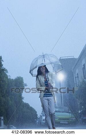 Happy woman with umbrella walking in rain View Large Photo Image Stock Photograph - Happy woman with umbrella walking in rain. Fotosearch