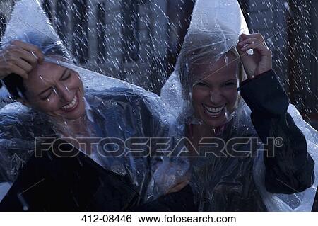 Stock Photograph - Laughing businesswomen wearing ponchos in rain. Fotosearch