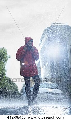 Stock Image - Man in raincoat walking in rainy street. Fotosearch