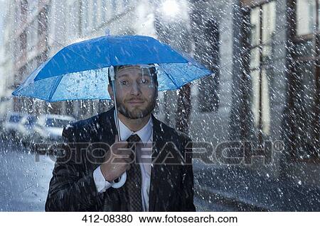 Stock Image - Portrait of businessman with tiny umbrella in rain. Fotosearch