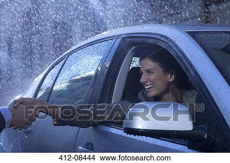 Picture - Smiling businesswoman in car extending handshake in rain. Fotosearch