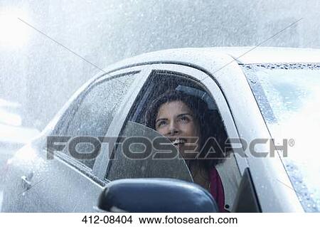 Picture - Smiling businesswoman in car looking up at rain. Fotosearch