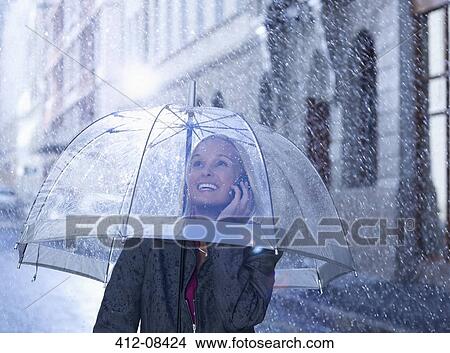 Smiling businesswoman talking on cell phone under umbrella in rainy street View Large Photo Image Picture - Smiling businesswoman talking on cell phone under umbrella in rainy street. Fotosearch