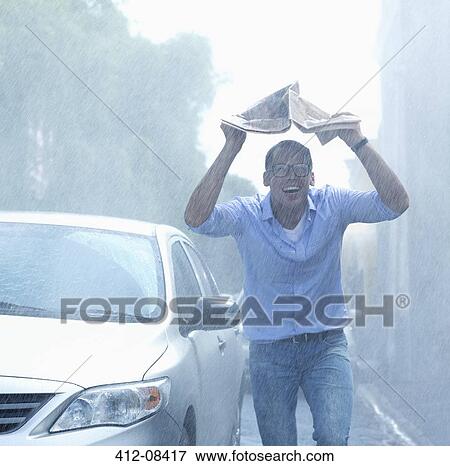 Smiling man holding newspaper overhead in rainy street View Large Photo Image Stock Photo - Smiling man holding newspaper overhead in rainy street. Fotosearch