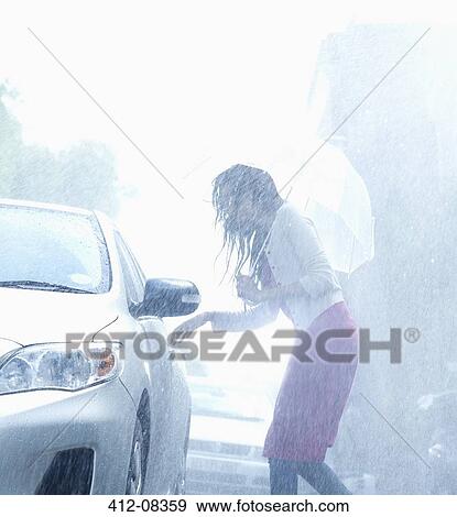 Stock Photo - Woman with umbrella reaching for car door handle in rain. Fotosearch