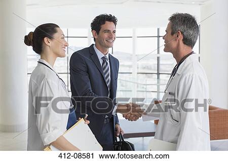 Doctor and businessman handshaking in hospital lobby View Large Photo Image Stock Image - Doctor and businessman handshaking in hospital lobby. Fotosearch