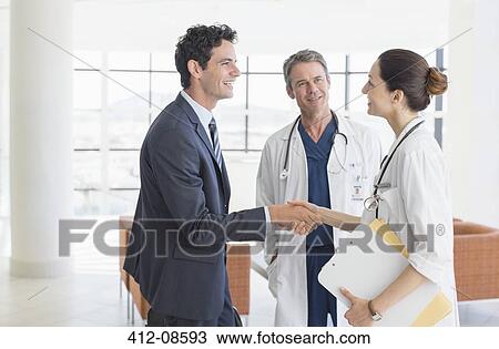 Stock Image - Doctor and businessman handshaking in hospital lobby. Fotosearch