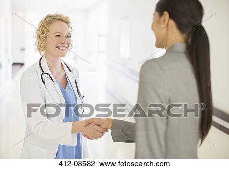 Stock Image - Doctor and businesswoman handshaking in hospital corridor. Fotosearch