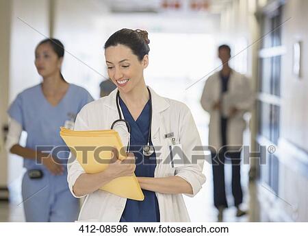 Stock Photograph - Doctor looking down at files in hospital corridor. Fotosearch