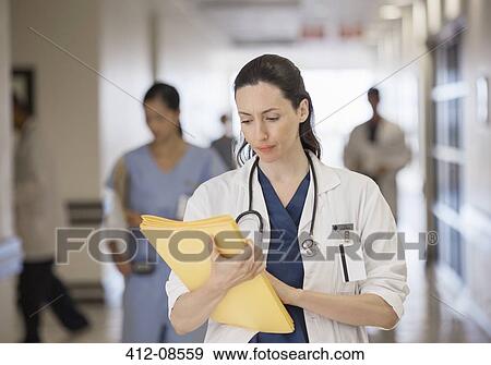 Stock Photo - Doctor looking down at folder in hospital corridor. Fotosearch