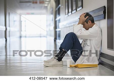 Doctor sitting on floor in hospital corridor with head in hands View Large Photo Image Stock Photo - Doctor sitting on floor in hospital corridor with head in hands. Fotosearch