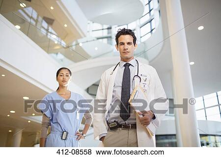 Portrait of confident doctor and nurse in hospital atrium View Large Photo Image Stock Photo - Portrait of confident doctor and nurse in hospital atrium. Fotosearch