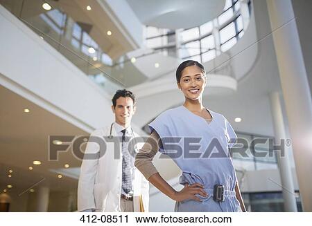 Stock Image - Portrait of smiling doctor and nurse in hospital atrium. Fotosearch