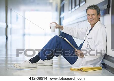 Portrait of smiling doctor drinking coffee on floor in hospital corridor View Large Photo Image Picture - Portrait of smiling doctor drinking coffee on floor in hospital corridor. Fotosearch