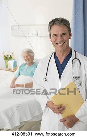 Stock Image - Portrait of smiling doctor with patient in background. Fotosearch