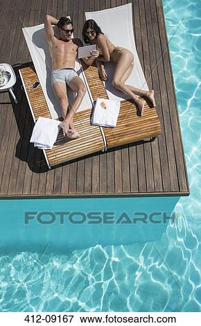 Couple relaxing on lounge chairs at poolside View Large Photo Image Stock Photo - Couple relaxing on lounge chairs at poolside. Fotosearch