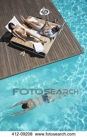 Stock Photo - Couple relaxing on lounge chairs at poolside. Fotosearch