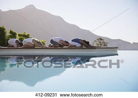 Stock Image - People practicing yoga at poolside. Fotosearch