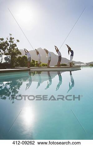 Stock Image - People practicing yoga at poolside. Fotosearch