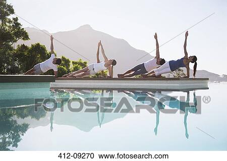 Stock Image - People practicing yoga at poolside. Fotosearch
