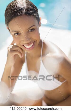 Stock Image - Smiling woman sitting poolside. Fotosearch