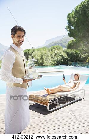 Stock Image - Waiter serving woman at poolside. Fotosearch
