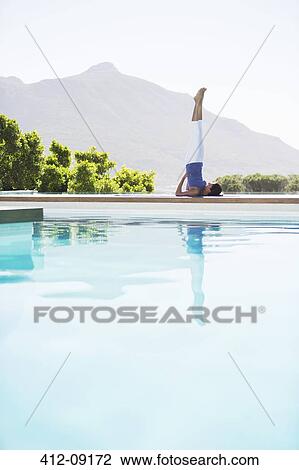 Stock Image - Woman practicing yoga at poolside. Fotosearch