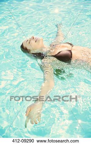 Stock Image - Woman relaxing on back in swimming pool. Fotosearch