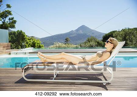 Stock Image - Woman relaxing on lounge chair at poolside. Fotosearch