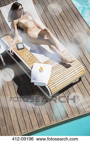 Woman relaxing on lounge chair at poolside View Large Photo Image Stock Photograph - Woman relaxing on lounge chair at poolside. Fotosearch
