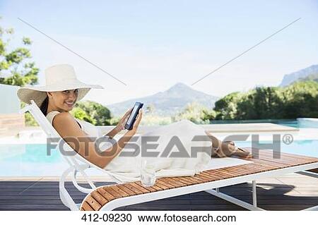 Woman using digital tablet on lounge chair at poolside View Large Photo Image Stock Image - Woman using digital tablet on lounge chair at poolside. Fotosearch