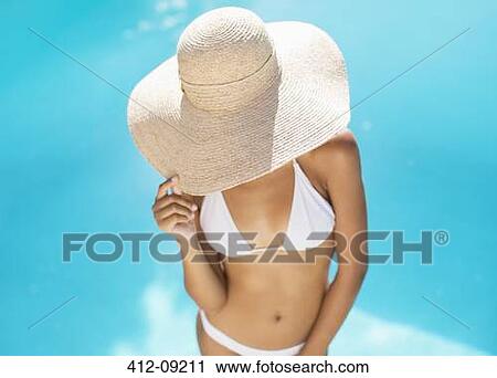Stock Image - Woman wearing straw hat at poolside. Fotosearch