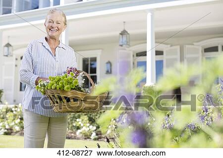Stock Photo - Portrait of senior woman picking flowers in garden. Fotosearch