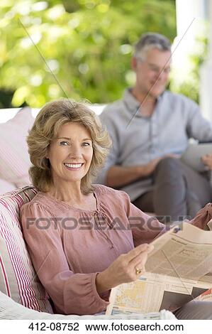 Stock Image - Portrait of senior woman reading newspaper on patio. Fotosearch