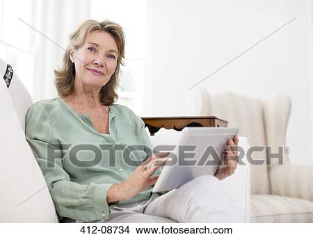 Portrait of senior woman using digital tablet on sofa View Large Photo Image Picture - Portrait of senior woman using digital tablet on sofa. Fotosearch