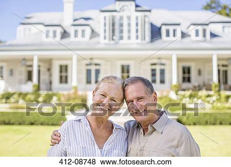 Stock Photo - Portrait of smiling senior couple in front of house. Fotosearch