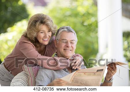 Stock Photography - Senior couple reading newspaper on patio. Fotosearch