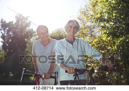 Senior couple walking bicycles in park View Large Photo Image Picture - Senior couple walking bicycles in park. Fotosearch